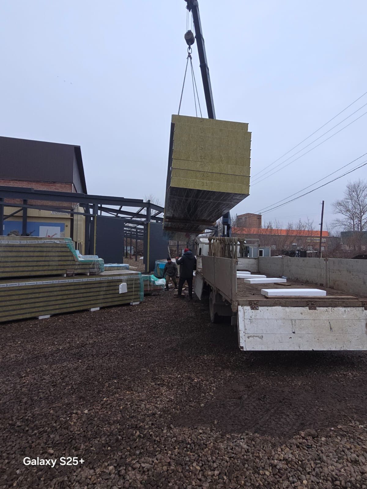 Кран подаёт пакет сэндвич-панелей на площадку